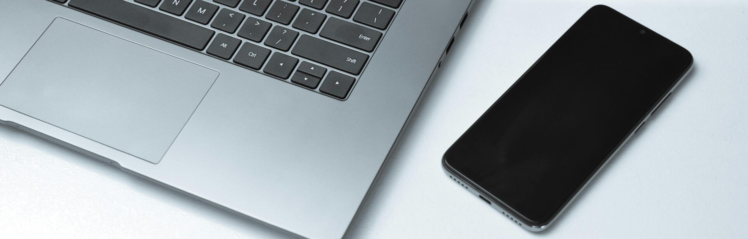 From above of contemporary netbook and cellphone with black screen on white desk